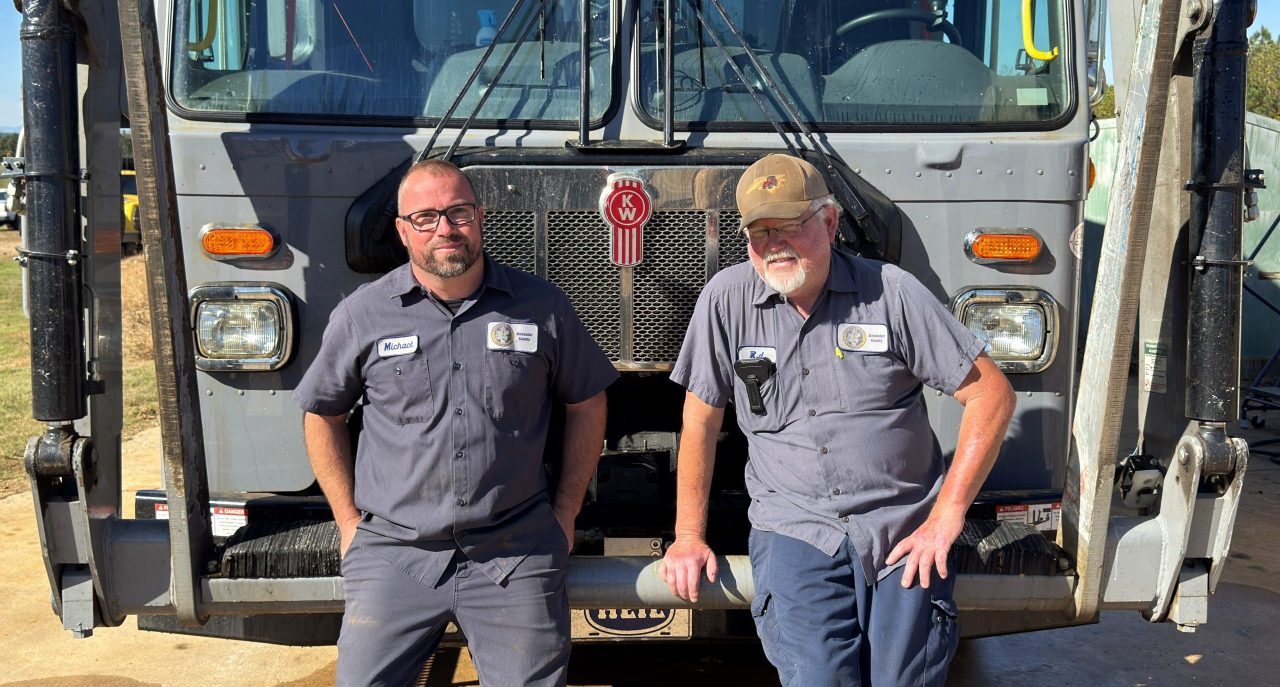 Michael Bare and RD Story sitting on the front end of a trash truck.