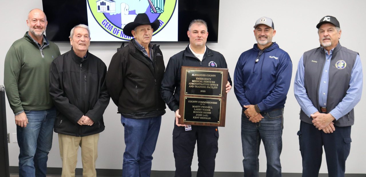 Alexander County Commissioners and EMS Director Jeff Sigmon stand in a line with a plaque commemorating the grand opening of the new EMS expansion.