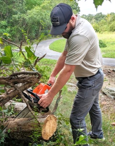 Joey Petriella uses a chainsaw to cut a fallen tree.