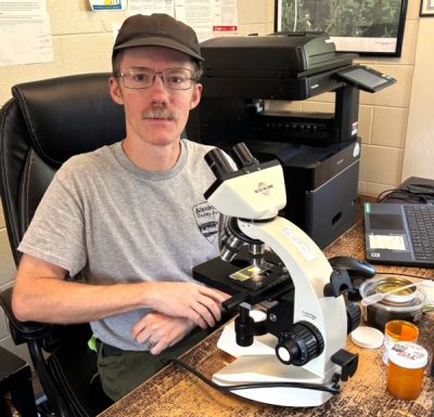 Robert Russo sits at a desk with his microscope.